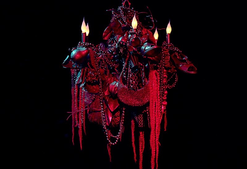 Scott N Andrew, Phase Shift. A dark, ornate chandelier-like sculpture with red lighting, adorned with beads, chains, and cand