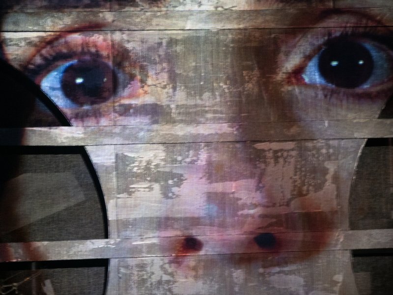 Close-up of a person's eyes and nose, partially obscured by horizontal, distressed white and gray bars.