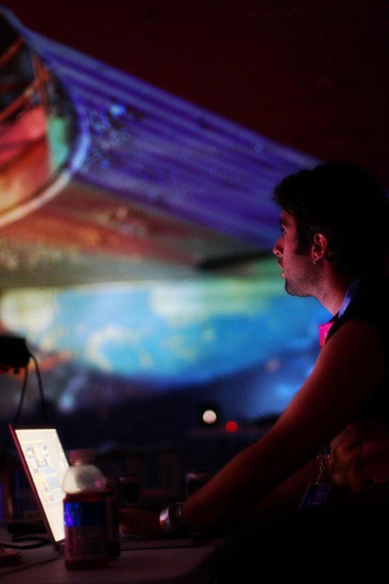 Man in profile, looking at a laptop, with colorful projected light illuminating a dark room.