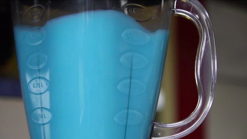 Close-up of a blender filled with bright blue liquid, showing measurement markings on the side and a clear handle.