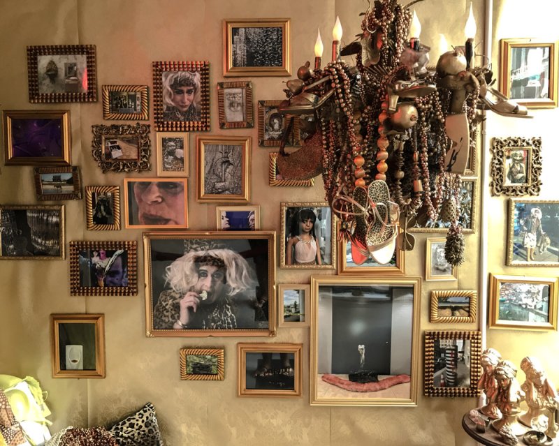 A wall covered in ornate gold-framed pictures, with a large, elaborate chandelier on the right.