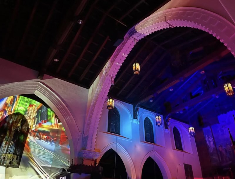 Church interior with white arches, hanging lanterns, and colorful projections on walls and ceiling.