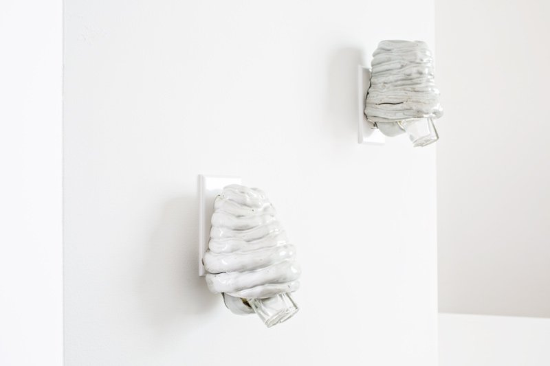 Two white, lumpy ceramic sculptures resembling melting soft-serve ice cream, plugged into a white wall.