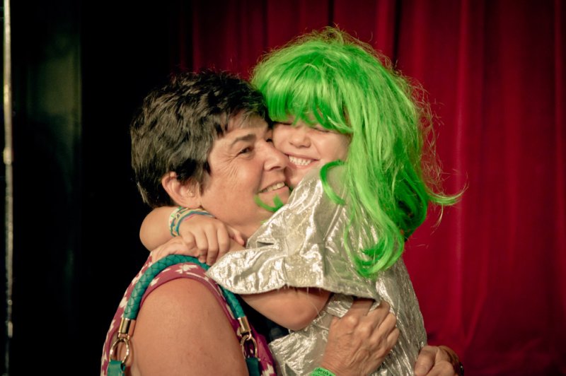 A woman with short dark hair hugs a child in a silver costume and bright green wig, both smiling.