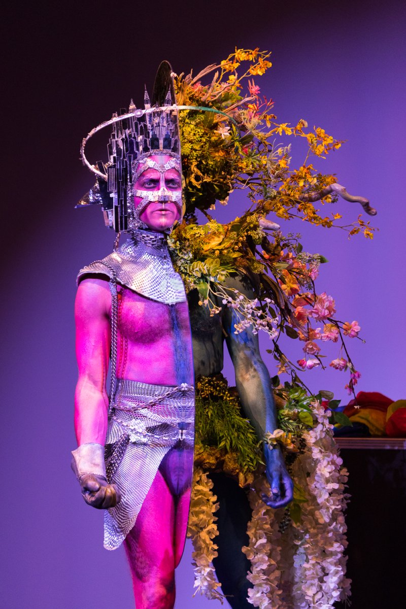 Drag performer Darrell Thorne in a split costume: half metallic warrior with a city skyline crown, half nature spirit with flowers.