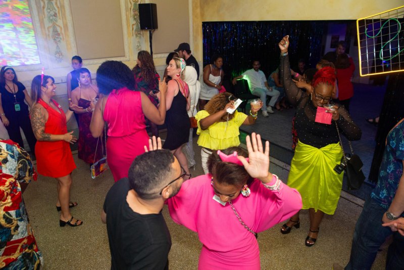 Diverse group of people dancing at a party, vibrant clothing, colorful lighting, festive atmosphere.