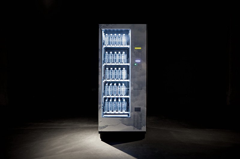 A dark, minimalist photo of a vending machine filled with water bottles, illuminated from within against a black background.