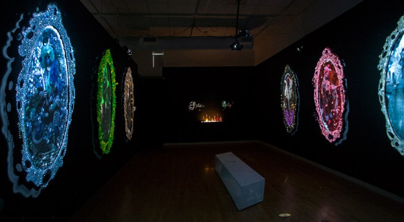 Dark room with projected oval frames on walls, displaying colorful, ornate digital art. A bench sits in the center.