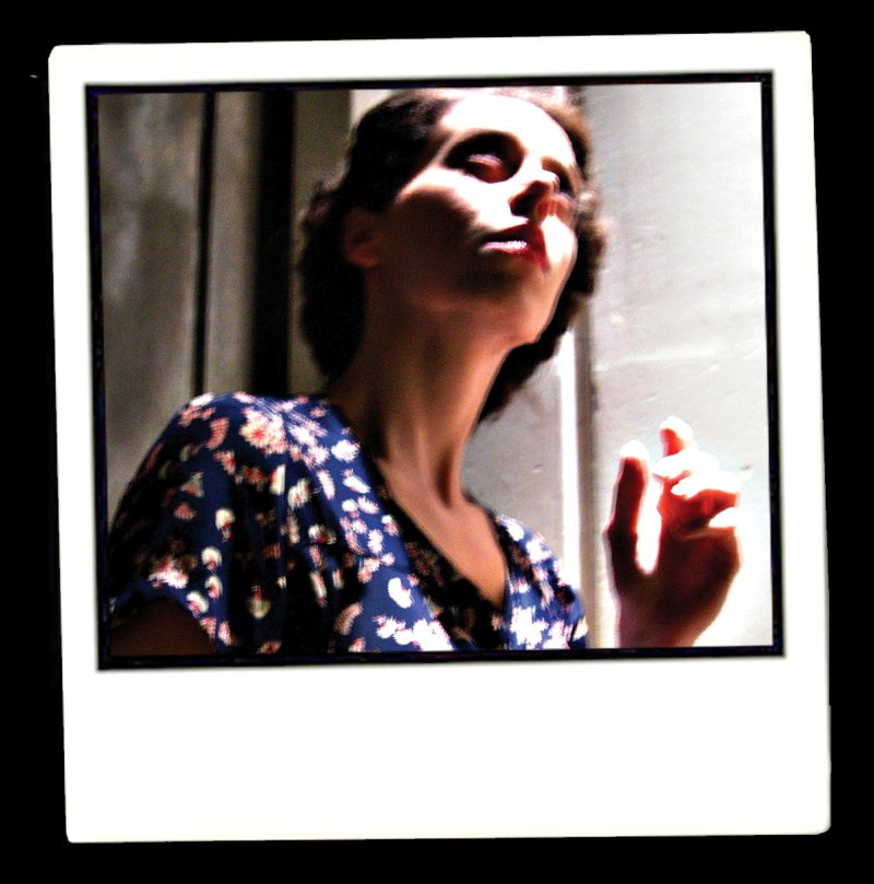 Polaroid of a woman in a floral dress, head tilted back, eyes closed, with dramatic lighting creating strong shadows and highlights.