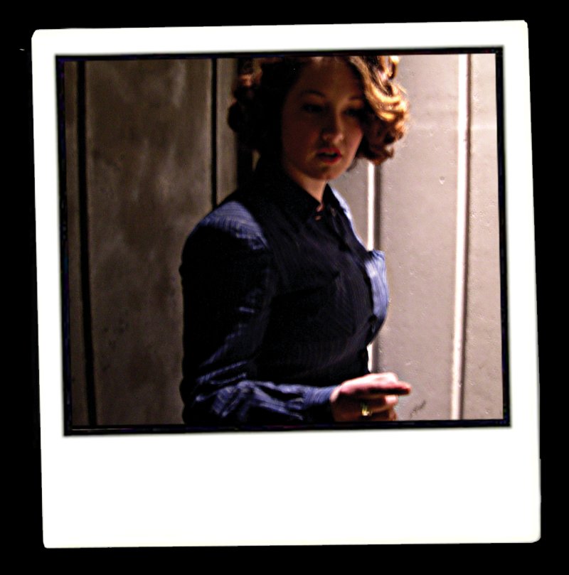 Polaroid of a woman with auburn hair in a dark blue shirt, facing right, against a muted brown background.
