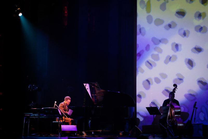 Scott N Andrew's "Suite Life" (2022-2023) features a pianist and cellist on a dark stage, with abstract purple and white projections.