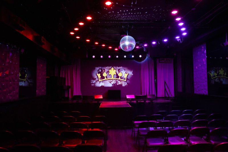 Dark stage with a disco ball, red and purple lights, and a projected golden crown logo on a white screen.