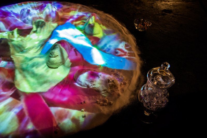Projected colorful light, including blue, pink, and green, on a mound of sugar with small sugar cubes.