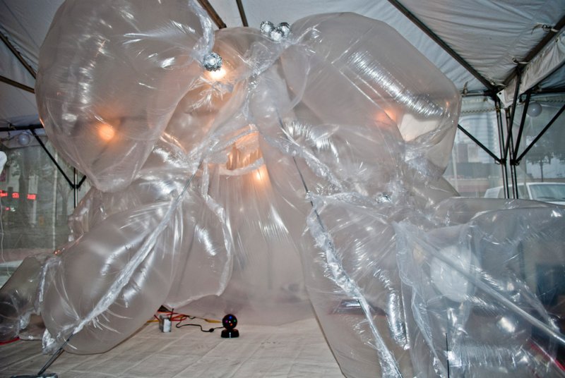 Large, clear inflatable sculpture with internal lights, filling a white tent space, with visible structural supports.