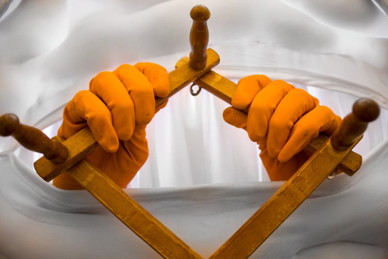 Two orange-gloved hands hold wooden tools, forming a diamond shape against a white background.