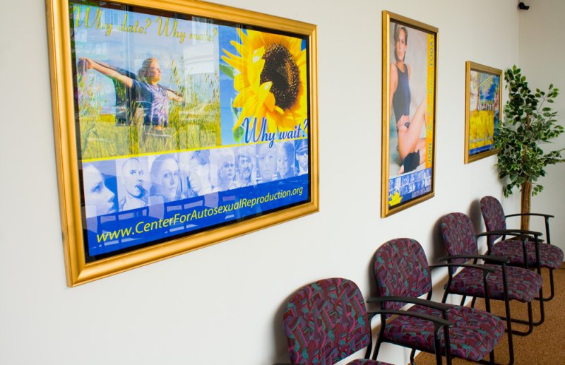 Three framed posters on a white wall above four patterned chairs, promoting "The Center For Autosexual Reproduction.