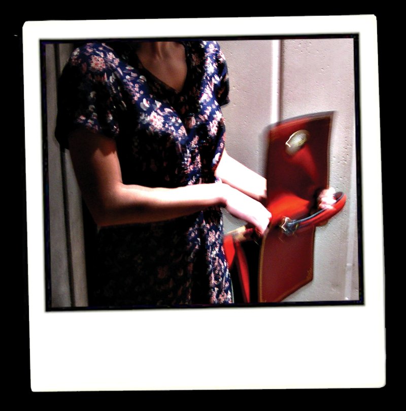 Woman in floral dress opening a red theater seat, captured in a blurred, candid style within a white polaroid frame.
