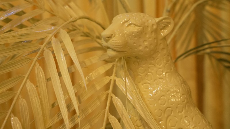 Monochromatic yellow-toned sculpture of a jaguar head and shoulder, surrounded by palm fronds.