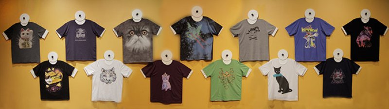Twelve unique cat-themed t-shirts, arranged in two rows against a warm yellow wall, showcasing diverse styles and colors.