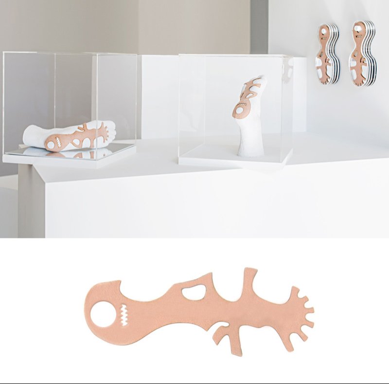 White sculptures resembling feet with abstract peach-colored patterns, displayed in clear cases and on a white wall.