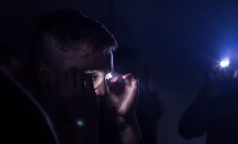 A person's face illuminated by a bright light reflecting in their eyes, with a second light source on the right.