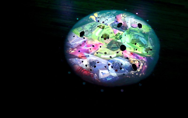 A glowing, colorful orb with geometric shapes and dark spots, against a dark background.