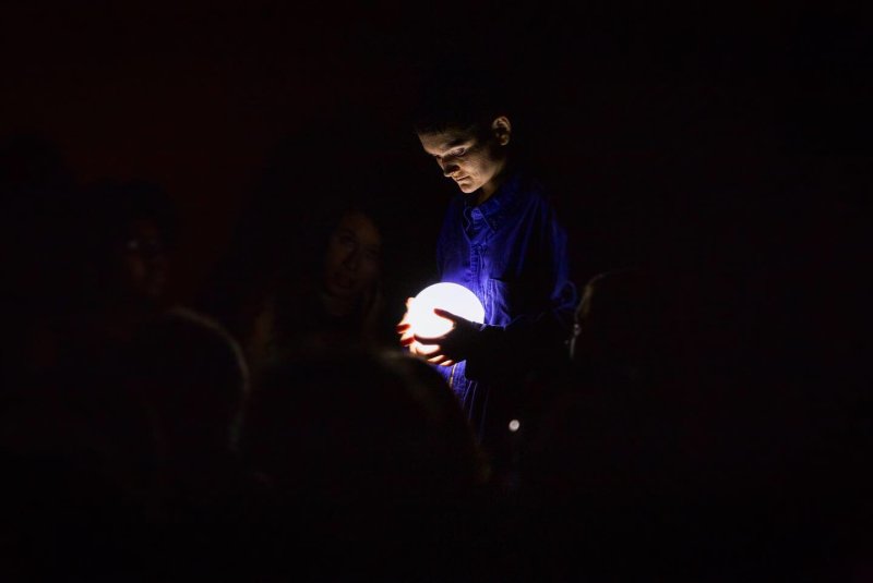 A person in a dark room holds a glowing white orb, illuminating their face and blue shirt.