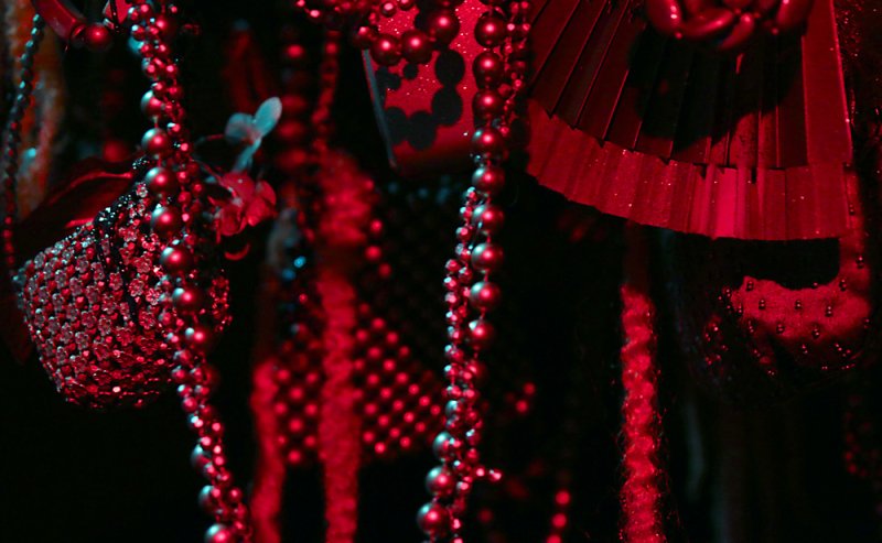 Close-up of red and black beaded strands, a red fan, and textured objects under dramatic red and blue lighting.