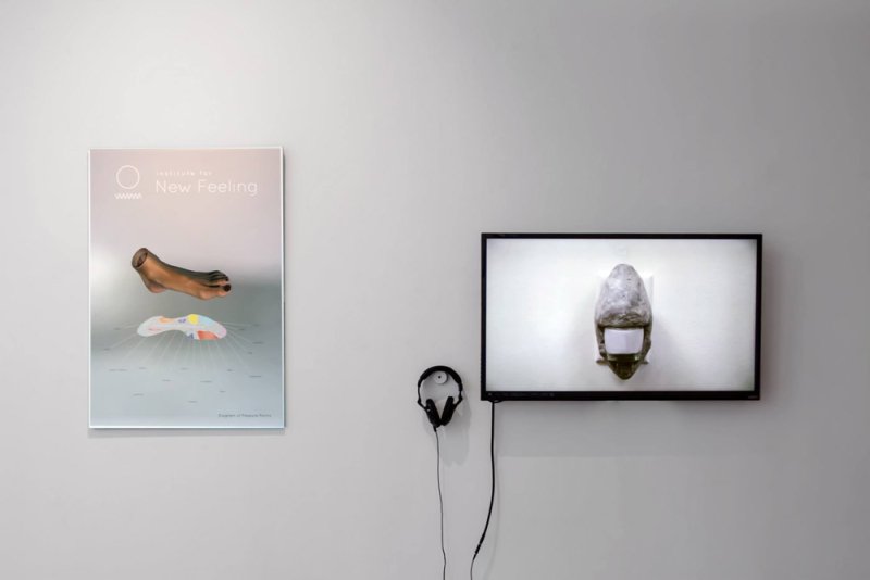 Poster of a detached foot and pressure points next to a TV screen displaying a stone-like object, with headphones hanging below.