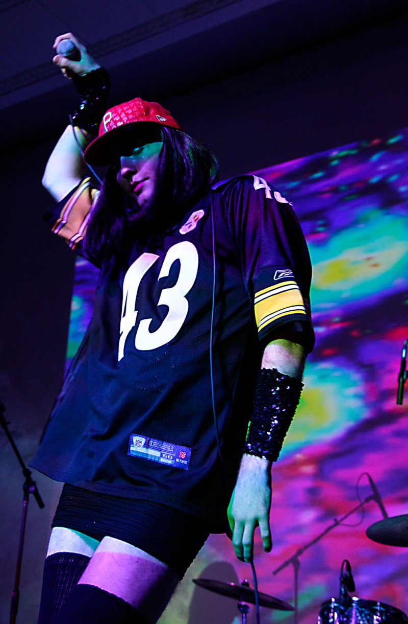 Performer in a #43 jersey and red cap, under blue and purple stage lights, against a colorful backdrop.