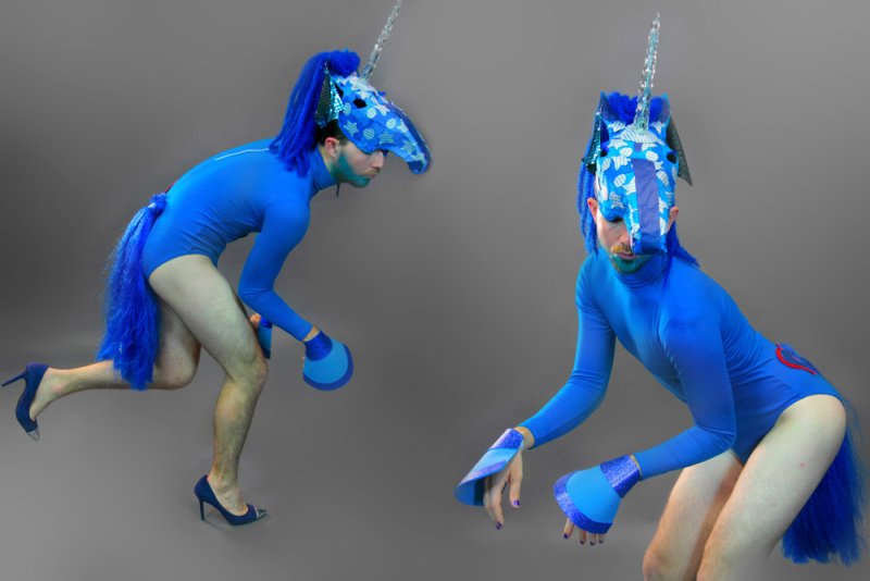 Two men in blue unicorn costumes with horse heads, tails, and hooves, against a gray background.