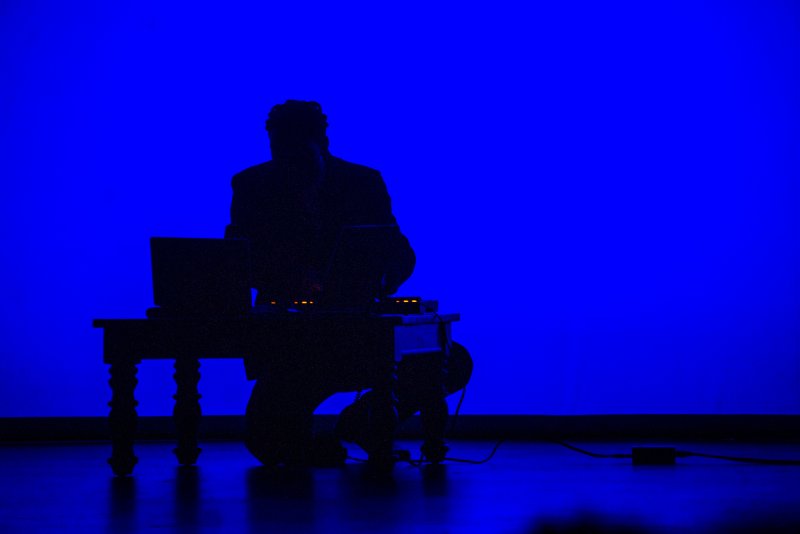 Silhouette of a person kneeling behind a table with laptops, against a vibrant blue background.