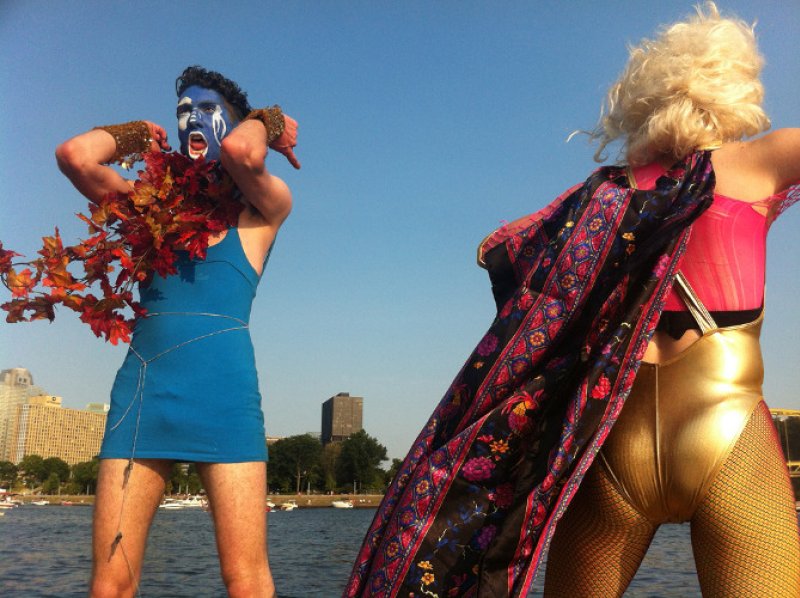 Two performers outdoors: one in blue with painted face and autumn leaves, the other in gold bodysuit, cape, and blonde wig.