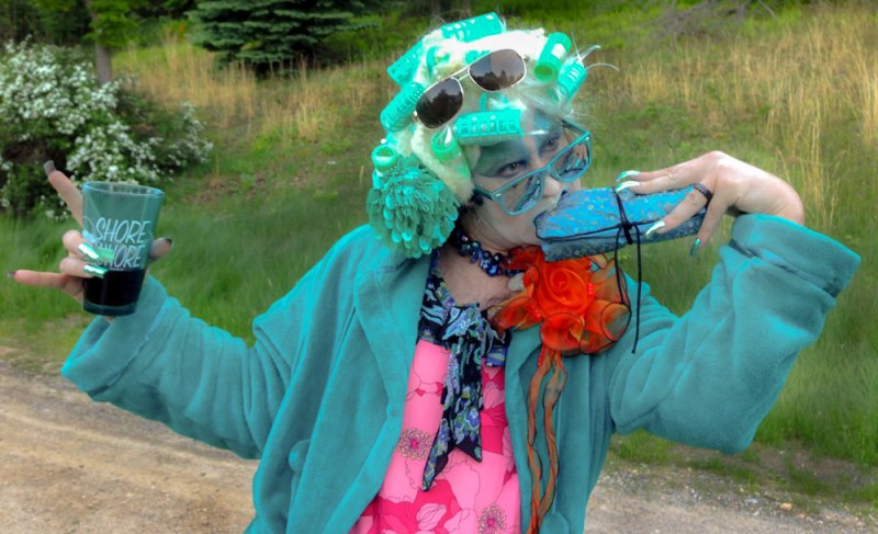 Scott N Andrew, Self Portraits. A person in a teal robe, pink dress, and blue curlers holds a drink and a clutch.