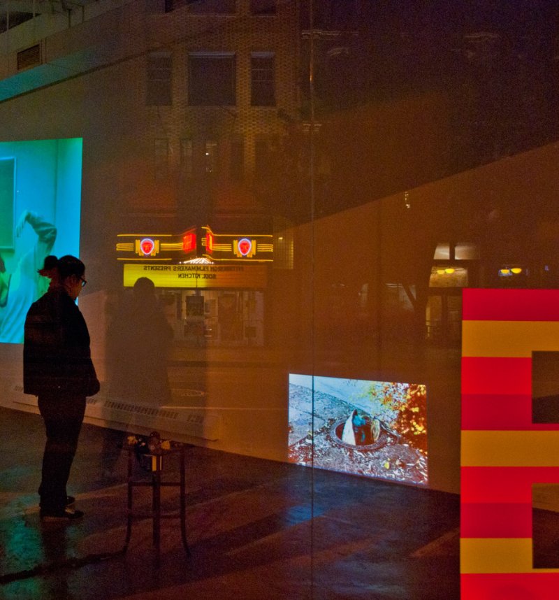 Woman viewing a multi-screen video installation with abstract shapes, a close-up eye, and a figure in a green room.