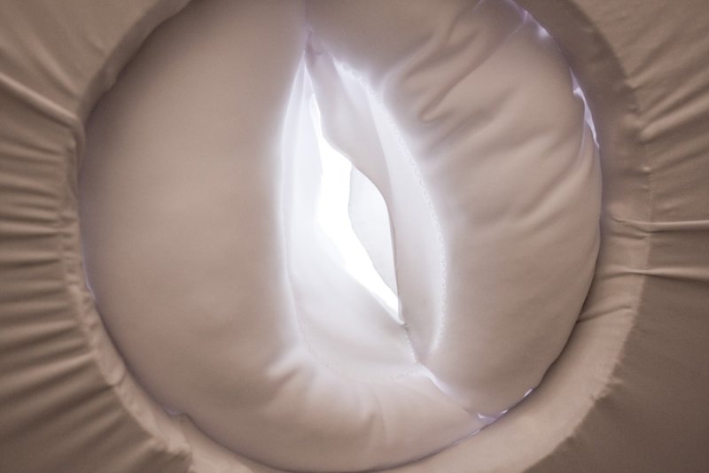 Soft, white fabric tunnel with a bright light at the end, viewed from a circular opening.