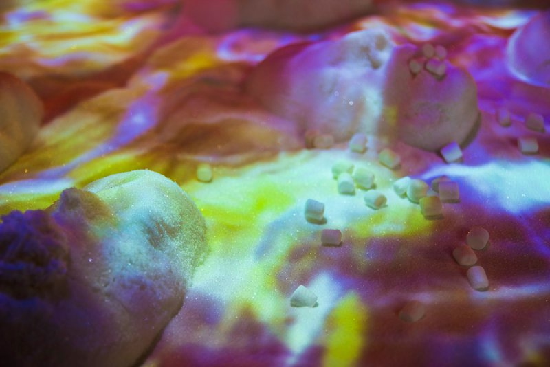 Close-up of white sugar mounds and scattered cubes under shifting yellow, purple, and blue light projections.