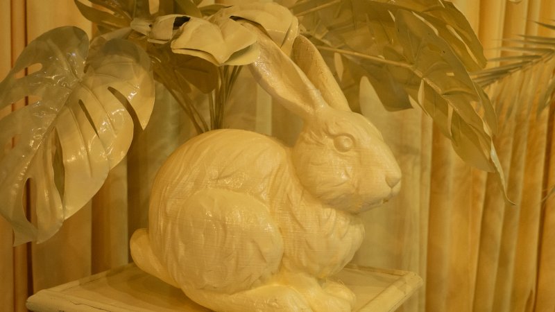 Monochromatic yellow sculpture of a rabbit surrounded by large leaves on a small table.