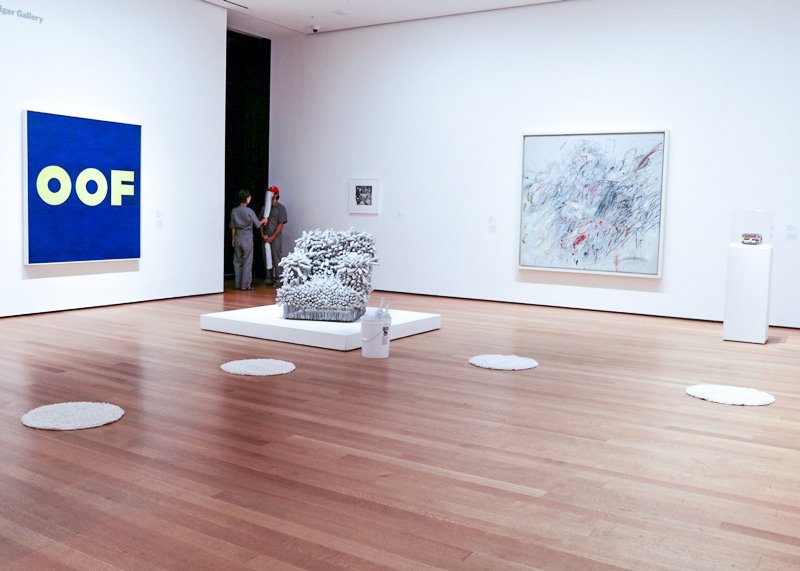 Modern art gallery with a blue "OOF" painting, a white textured sculpture, and an abstract drawing on white walls.