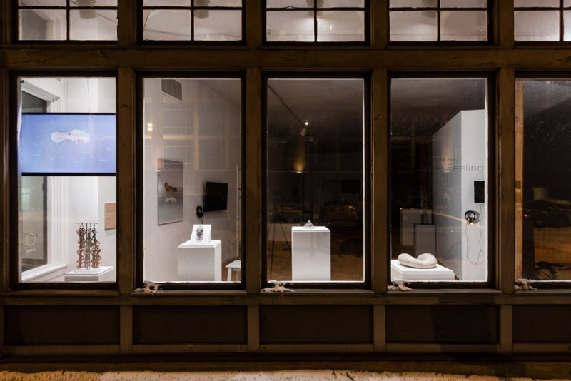 Gallery storefront at night with various sculptures and screens displayed in brightly lit windows.