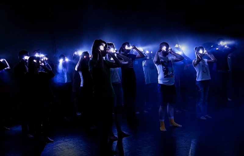 People in a dark room with bright blue lights illuminating their faces and hands, creating strong silhouettes.