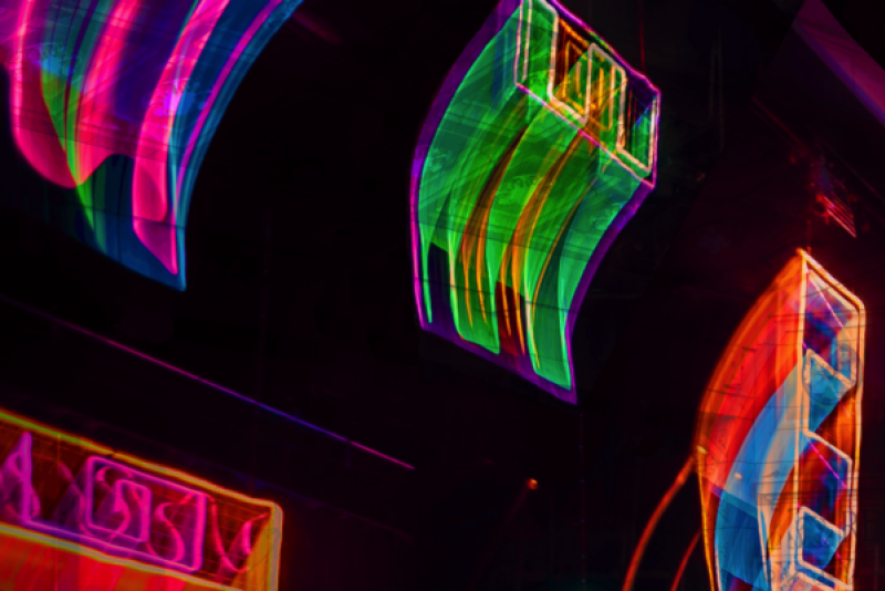 Abstract neon light art with glowing pink, green, and blue curved shapes against a dark background, creating a dynamic, blurred effect.