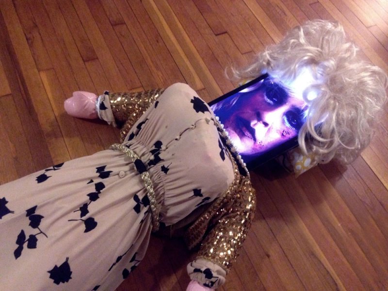 Mannequin in a floral dress and sequined jacket with a tablet for a head displaying a woman's face.